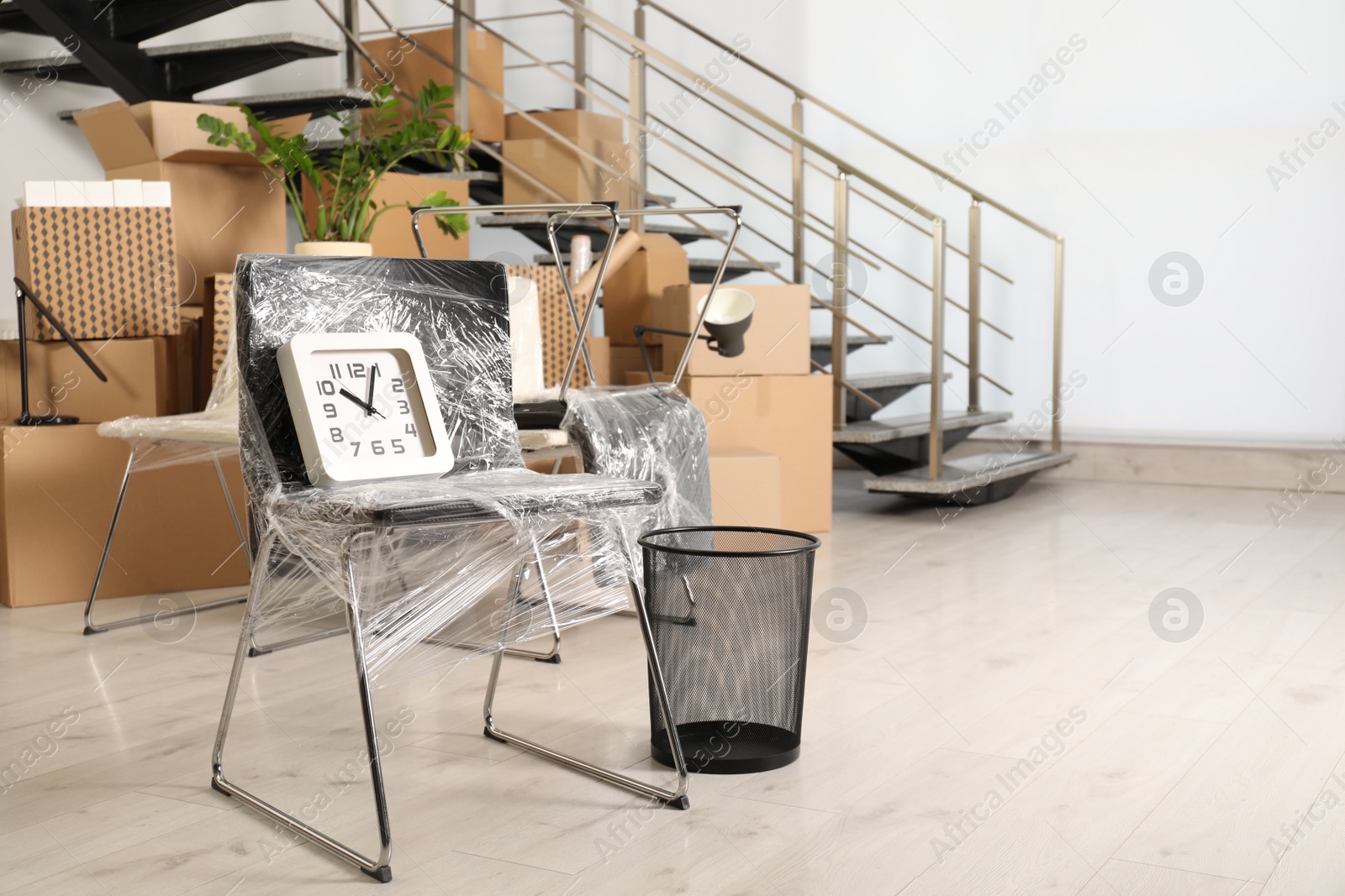 Photo of Packed chair, trash bin and clock near stairs in office, space for text. Moving day