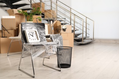 Packed chair, trash bin and clock near stairs in office, space for text. Moving day