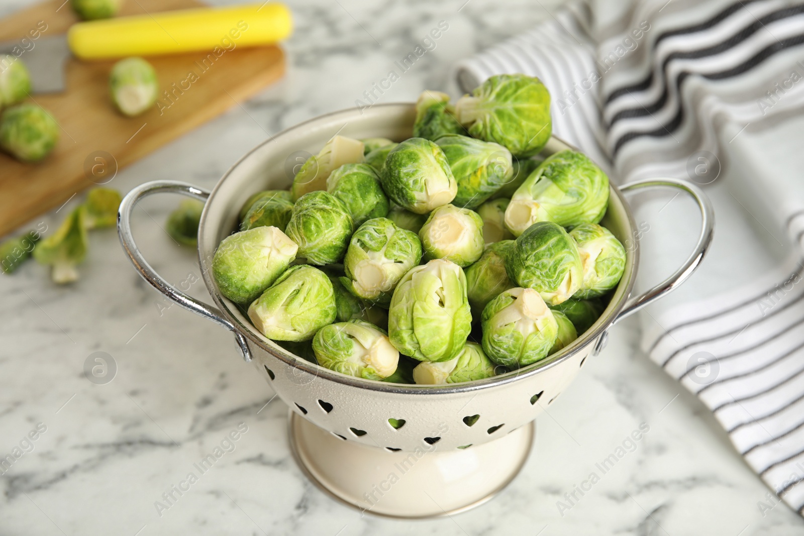 Photo of Colander with fresh Brussels sprouts on white marble table, closeup