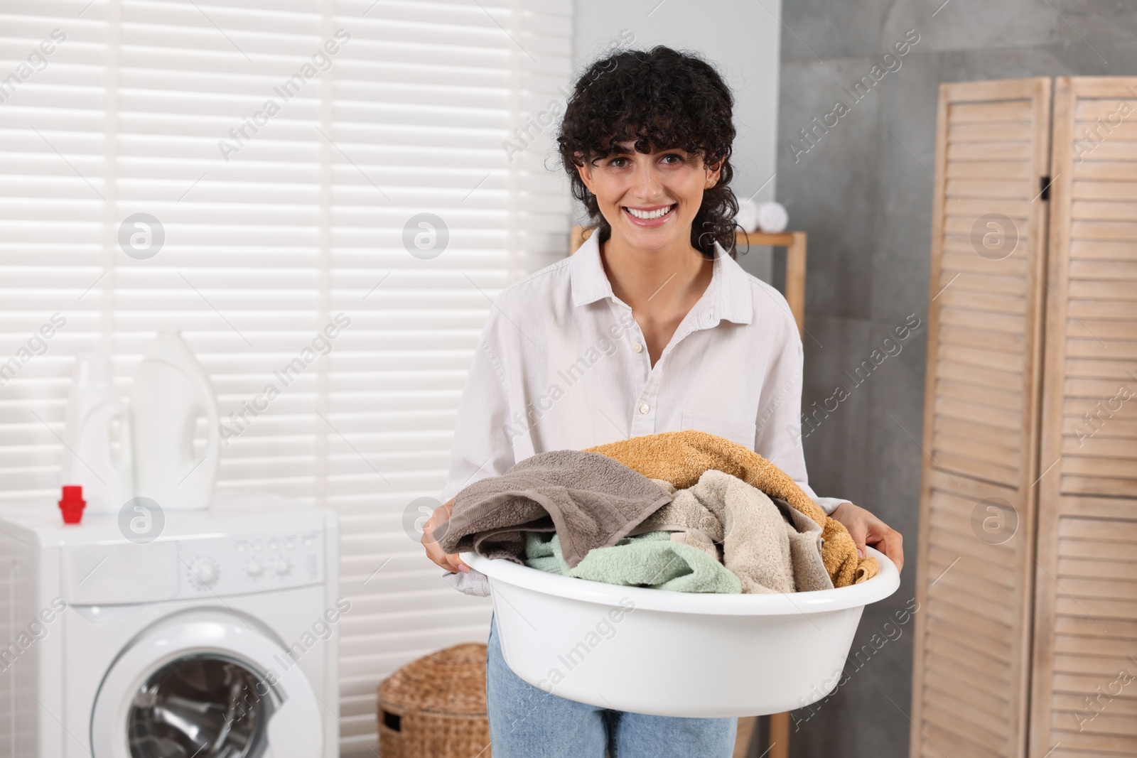 Photo of Happy woman holding basin with laundry indoors, space for text