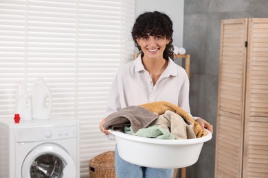Happy woman holding basin with laundry indoors, space for text