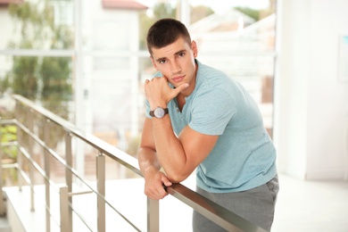 Portrait of handsome young man leaning on railing indoors