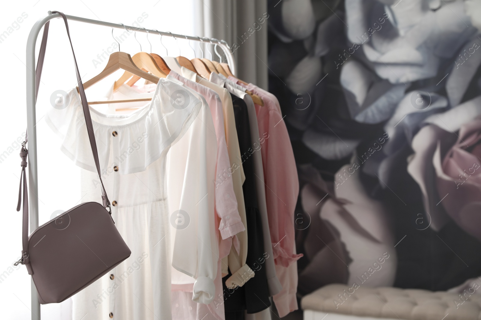 Photo of Rack with stylish women's clothes and handbag indoors. Interior design