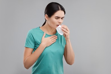 Woman with tissue coughing on grey background, space for text. Cold symptoms