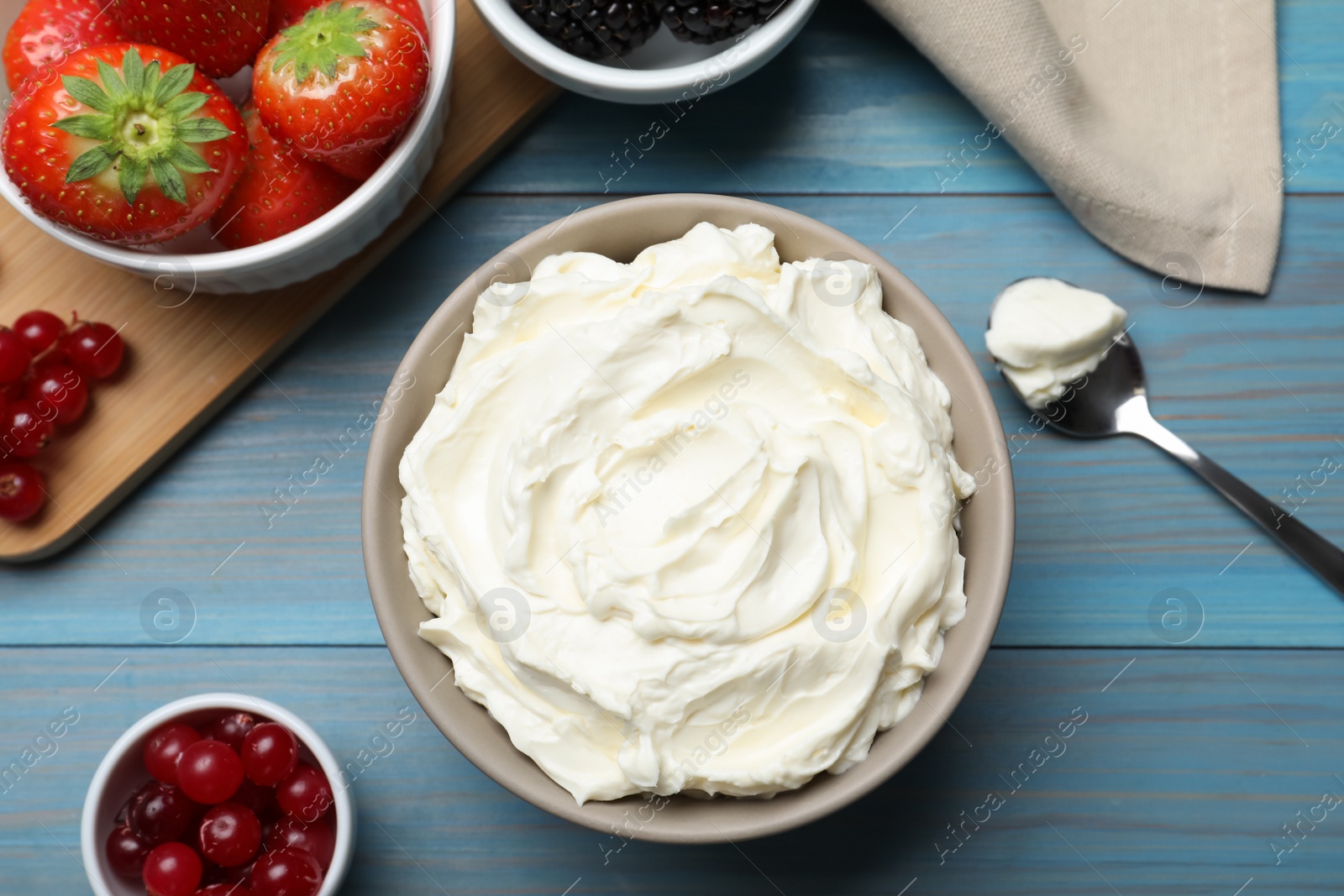 Photo of Tasty cream cheese and fresh berries on light blue wooden table, flat lay