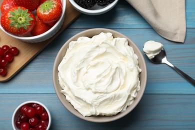 Photo of Tasty cream cheese and fresh berries on light blue wooden table, flat lay