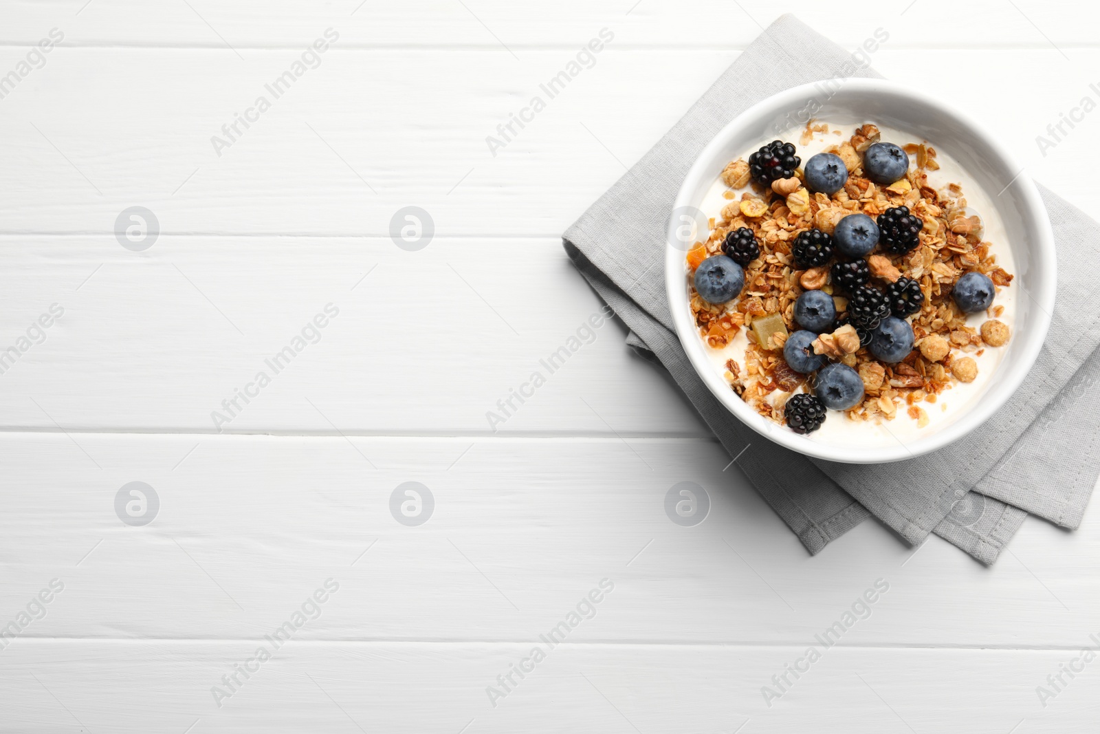 Photo of Bowl of healthy muesli served with berries on white wooden table, top view. Space for text