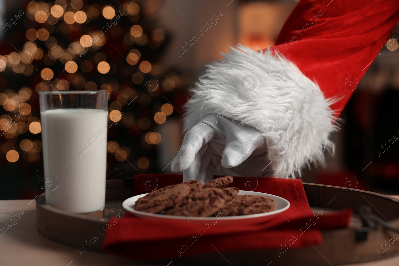 Photo of Merry Christmas. Santa Claus taking cookies from plate on table in room, closeup