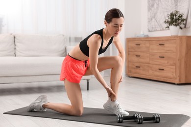 Photo of Young woman suffering from leg pain on exercise mat in room