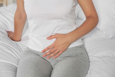 Photo of Young woman suffering from cystitis on bed, closeup