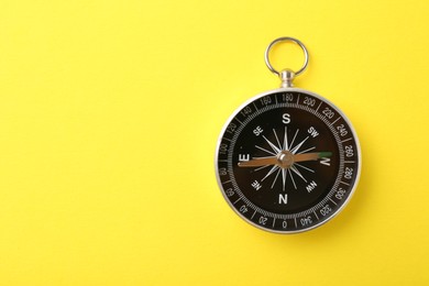 Photo of One compass on yellow background, top view and space for text. Tourist equipment