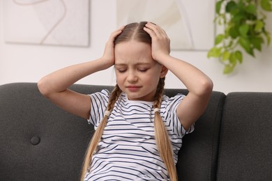 Photo of Little girl suffering from headache on sofa indoors