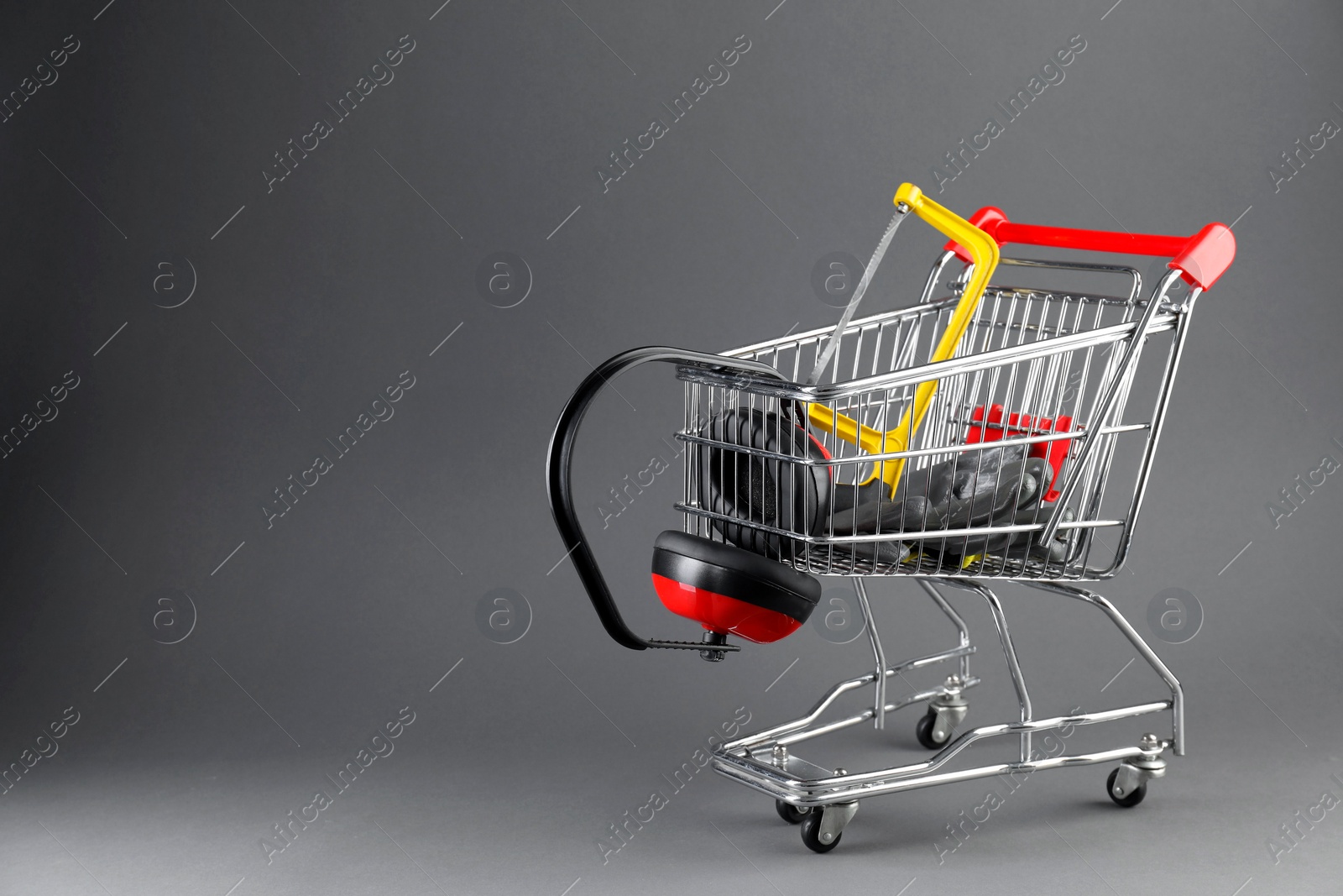 Photo of Small shopping cart with hacksaw, gloves and headphones on grey background. Space for text