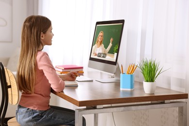 Image of E-learning. Little girl taking notes during online lesson at wooden table