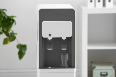 Modern water cooler with glass against blurred background