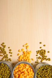 Photo of Open tin cans of conserved vegetables on wooden background, flat lay with space for text