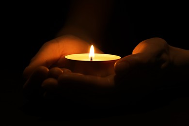 Woman holding burning candle in hands on black background, closeup