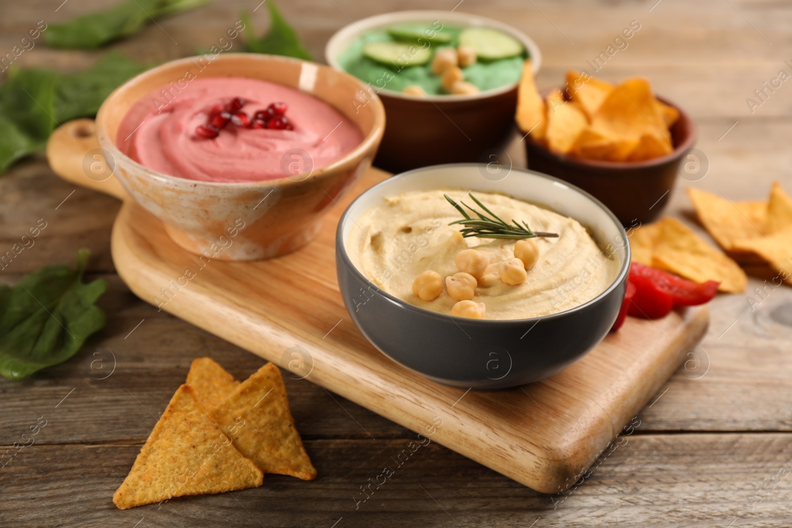 Photo of Different kinds of tasty hummus, nachos and ingredients on wooden table