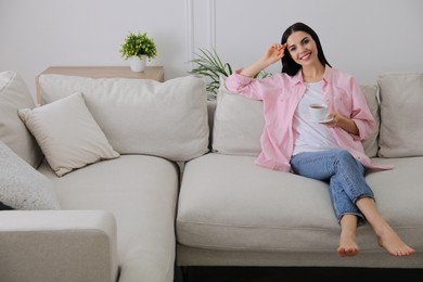 Photo of Woman with cup of drink resting on sofa in living room