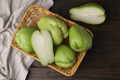 Photo of Cut and whole chayote in wicker basket on wooden table, flat lay