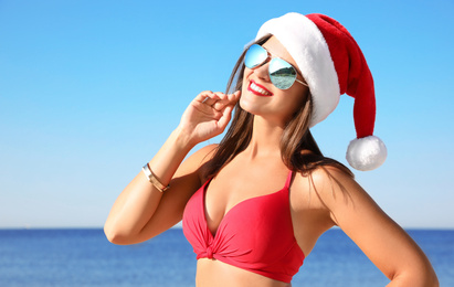 Photo of Young woman wearing Santa hat and bikini on beach. Christmas vacation