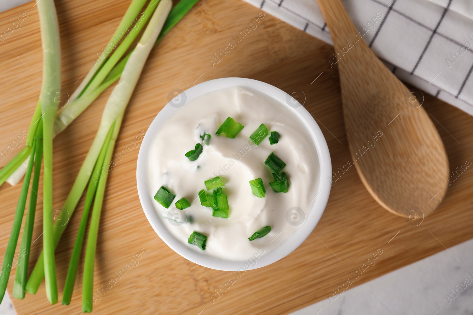 Photo of Fresh sour cream with onion on wooden board, top view