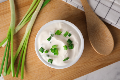 Photo of Fresh sour cream with onion on wooden board, top view