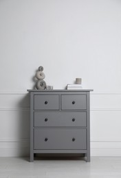 Different accessories on grey chest of drawers near white wall indoors