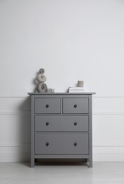 Photo of Different accessories on grey chest of drawers near white wall indoors