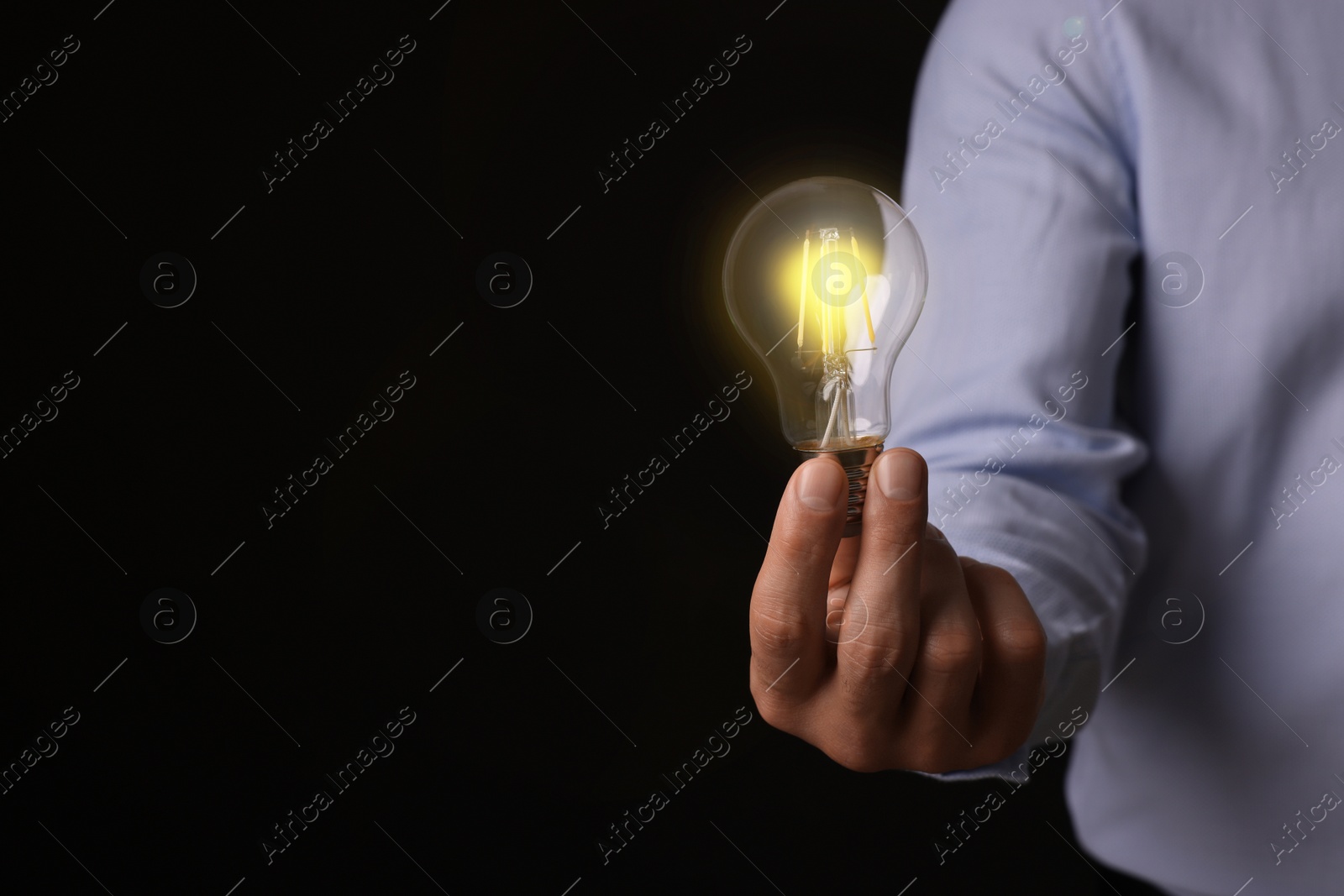 Photo of Glow up your ideas. Closeup view of man holding light bulb on black background, space for text