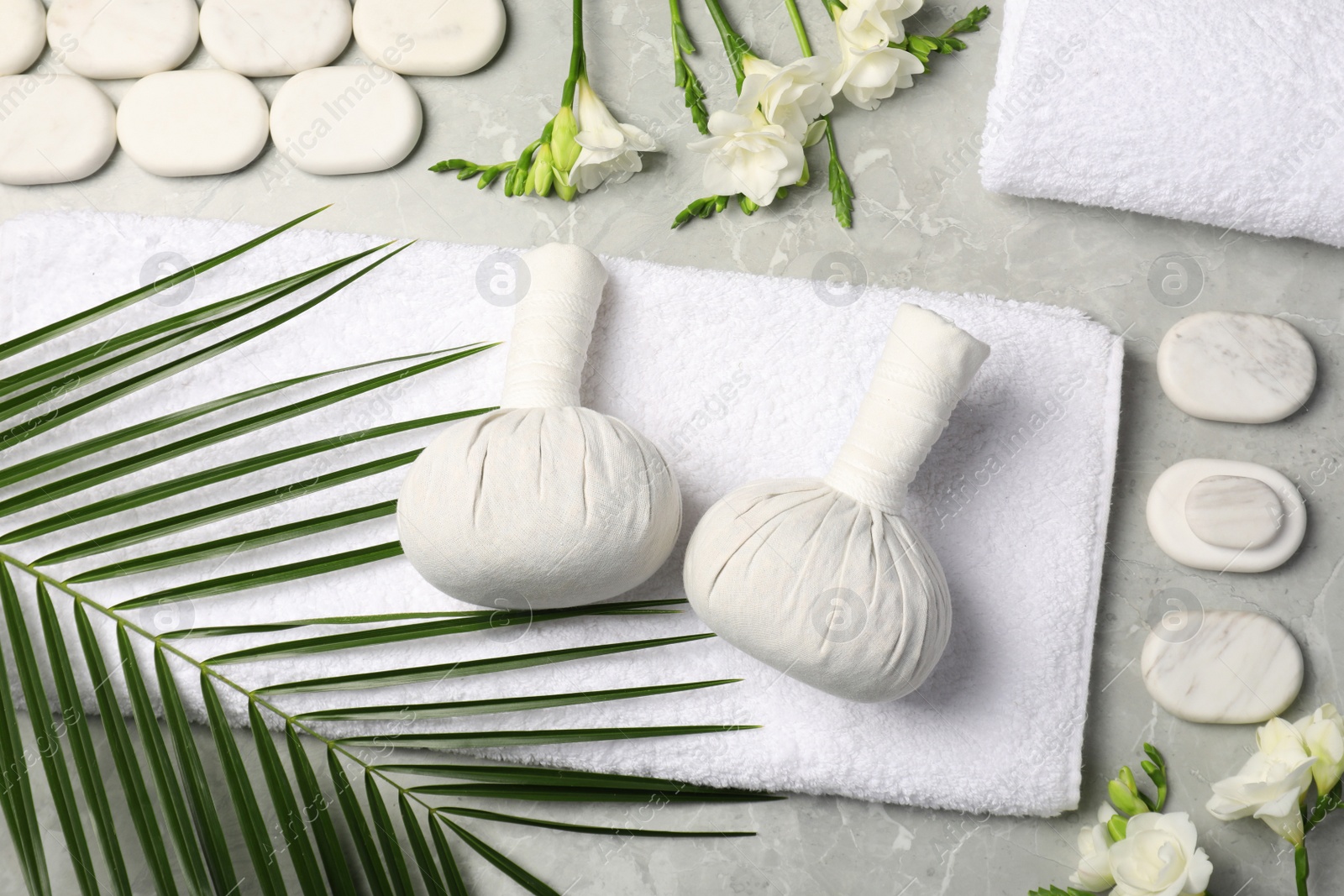 Photo of Spa bags, stones and freesia flowers on light gray marble table, flat lay