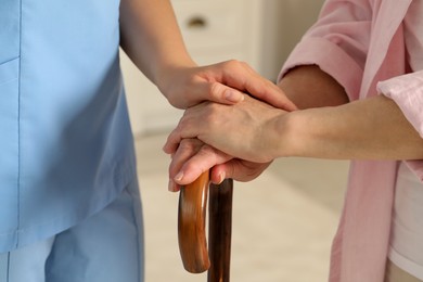 Elderly woman with walking cane and female caregiver indoors, closeup