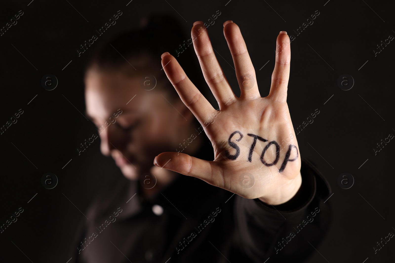 Photo of Woman with word Stop written on hand against dark background, closeup. Domestic violence concept