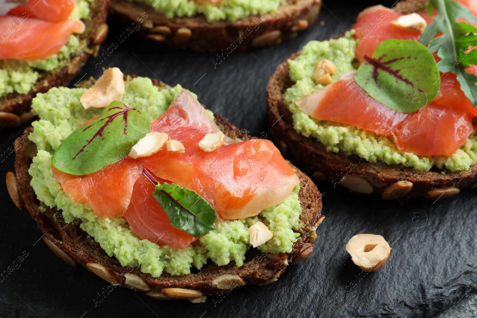 Photo of Delicious sandwiches with salmon, avocado and herbs on slate plate, closeup