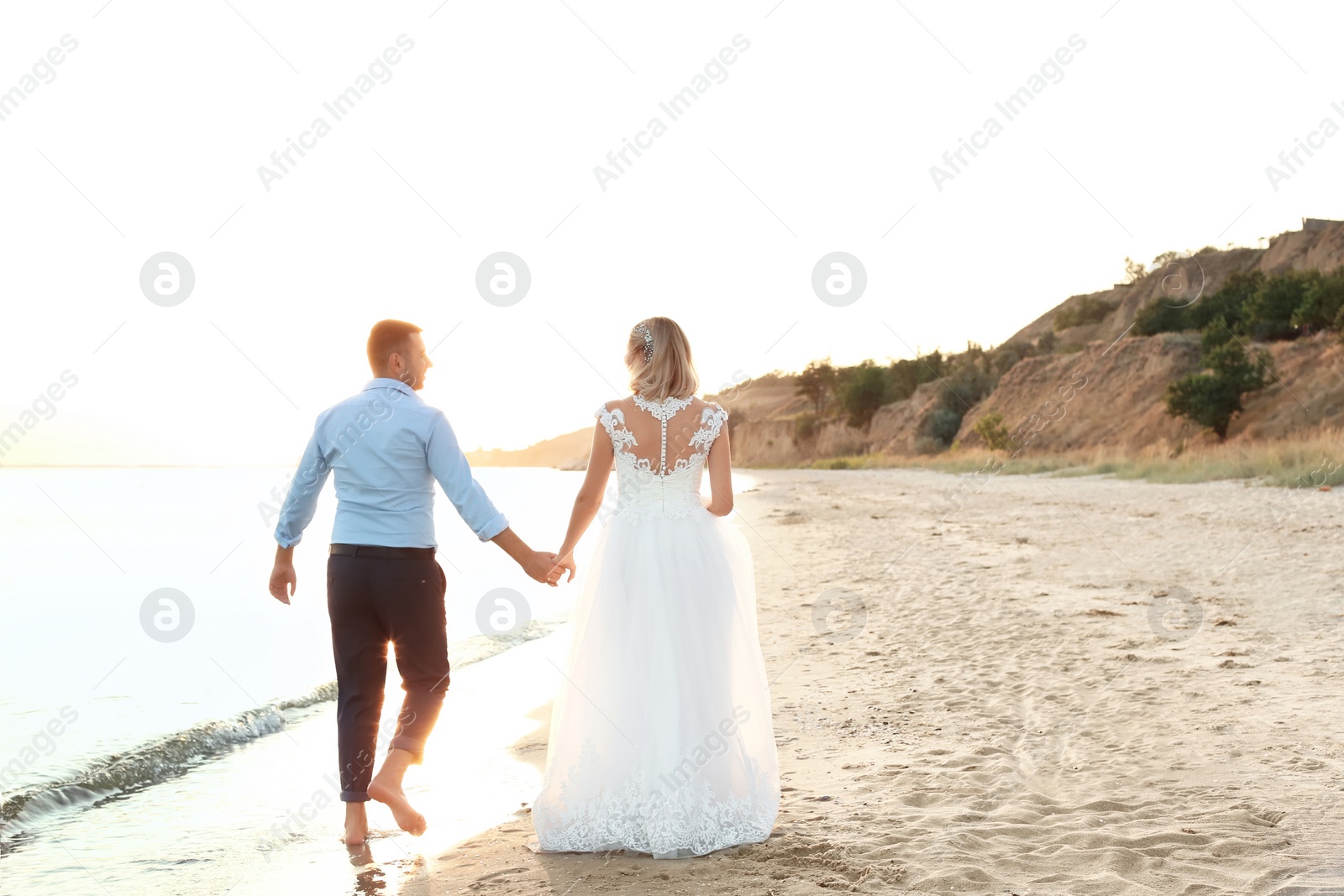 Photo of Wedding couple holding hands together on beach. Space for text