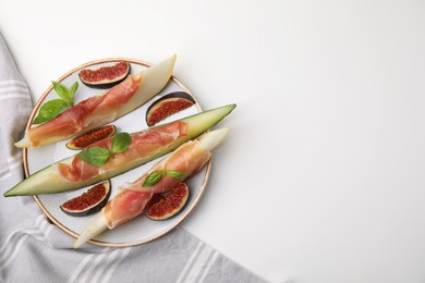 Photo of Plate of tasty melon, jamon, and figs on white table, top view. Space for text