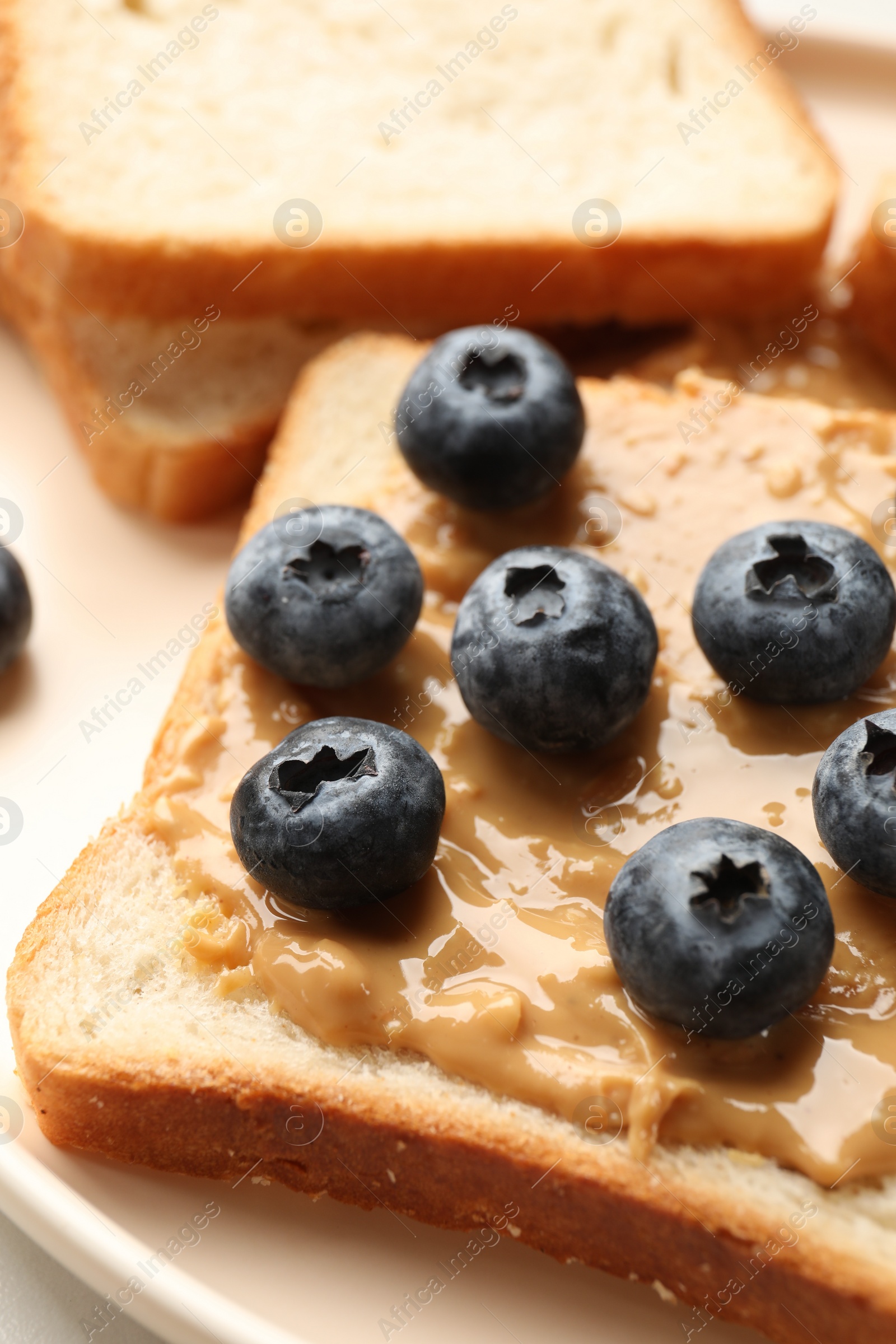 Photo of Delicious toasts with peanut butter and blueberries on plate, closeup