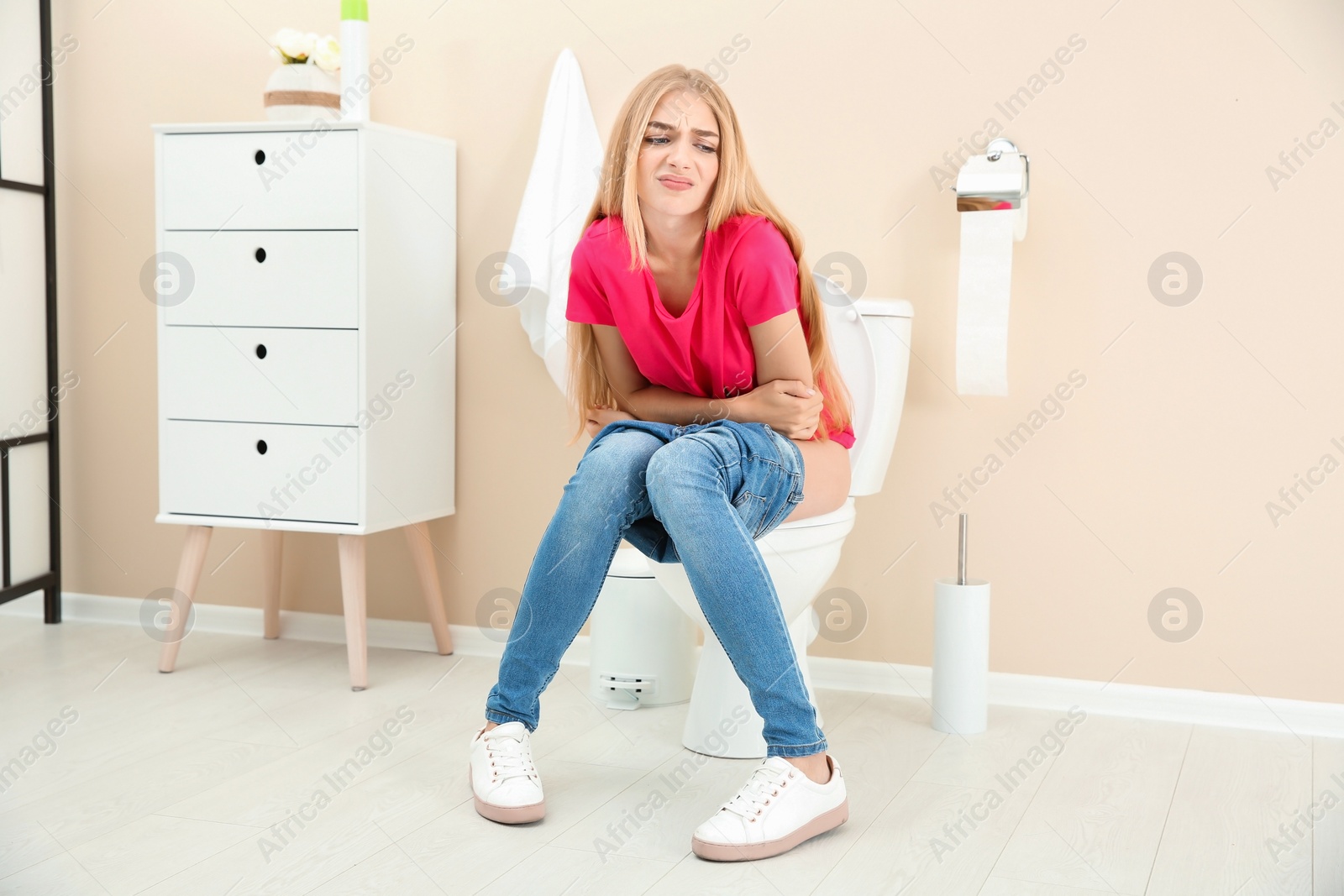 Photo of Young woman suffering from diarrhea on toilet bowl at home