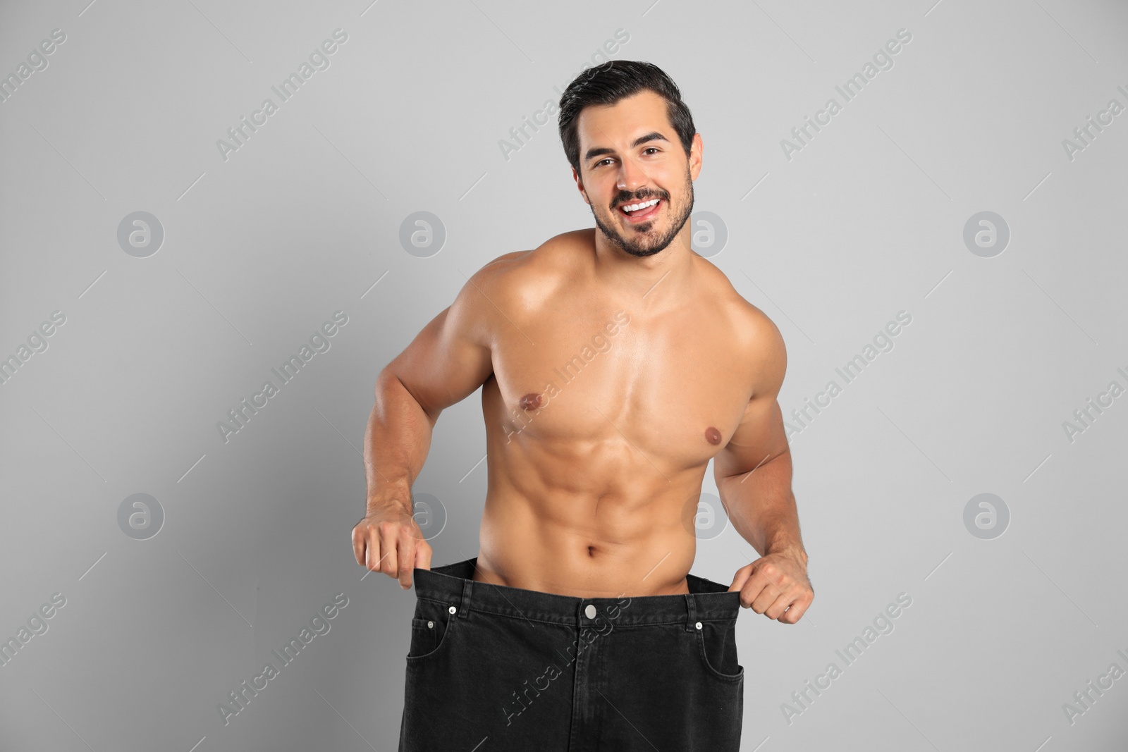 Photo of Young man with slim body in old big size jeans on grey background