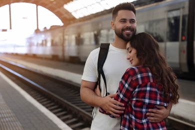 Long-distance relationship. Beautiful couple hugging on platform of railway station, space for text