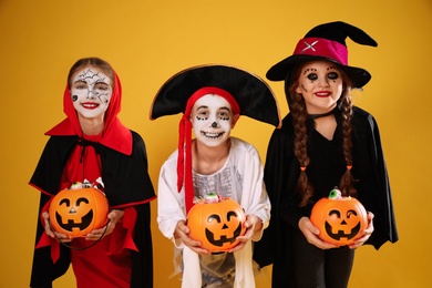 Photo of Cute little kids with pumpkin candy buckets wearing Halloween costumes on yellow background