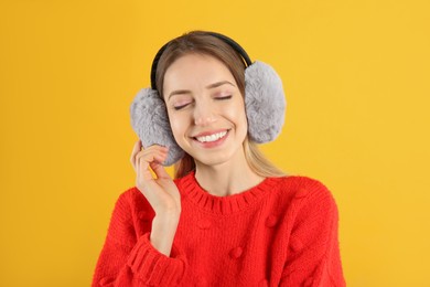 Photo of Happy woman wearing warm earmuffs on yellow background