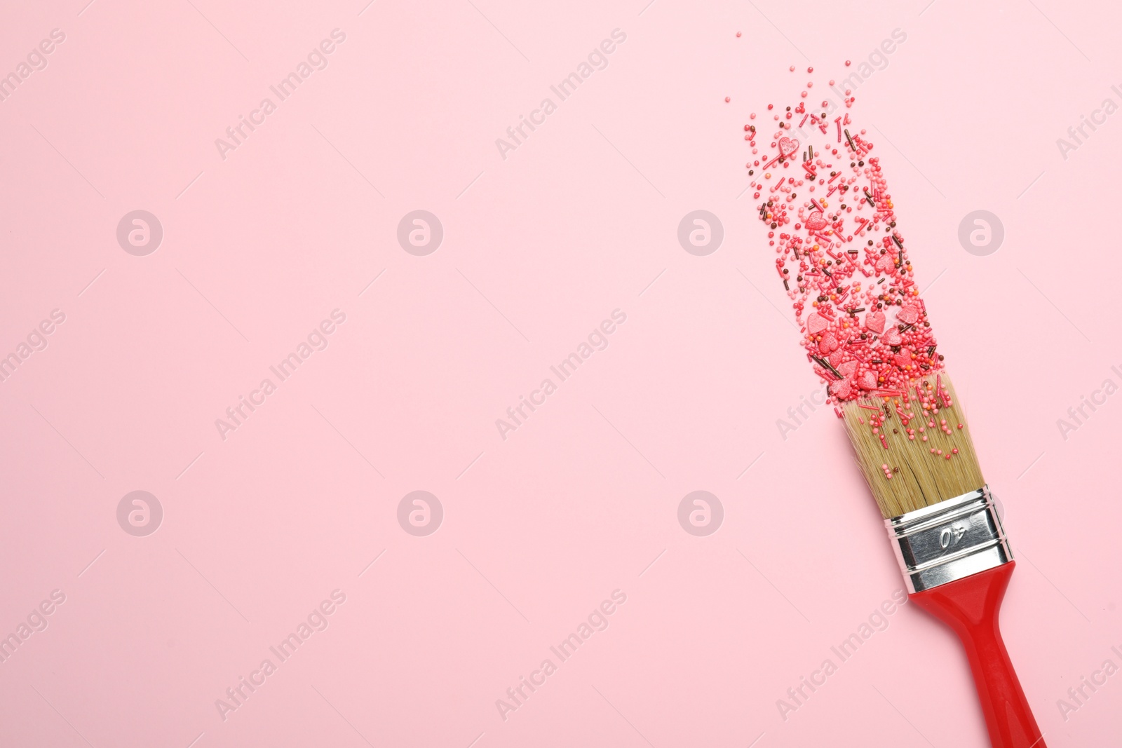 Photo of Brush painting with red sprinkles on pink background, top view. Space for text. Creative concept