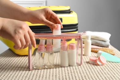 Photo of Woman putting small bottle with personal care product into plastic bag, closeup. Cosmetic travel kit