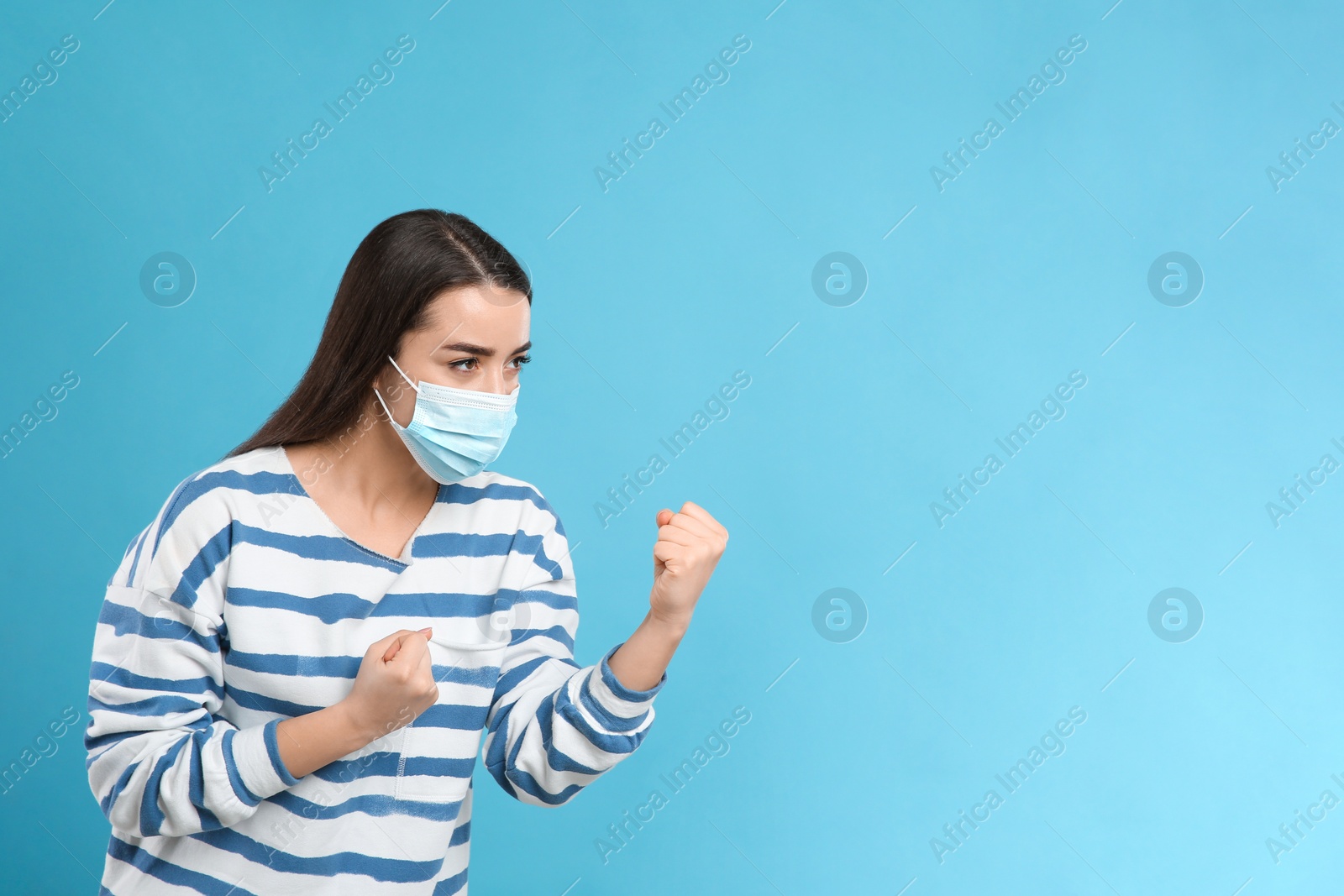 Photo of Woman with protective mask in fighting pose on light blue background, space for text. Strong immunity concept