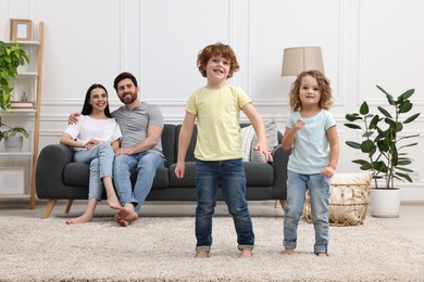 Photo of Happy children dancing while their parents looking at them in room