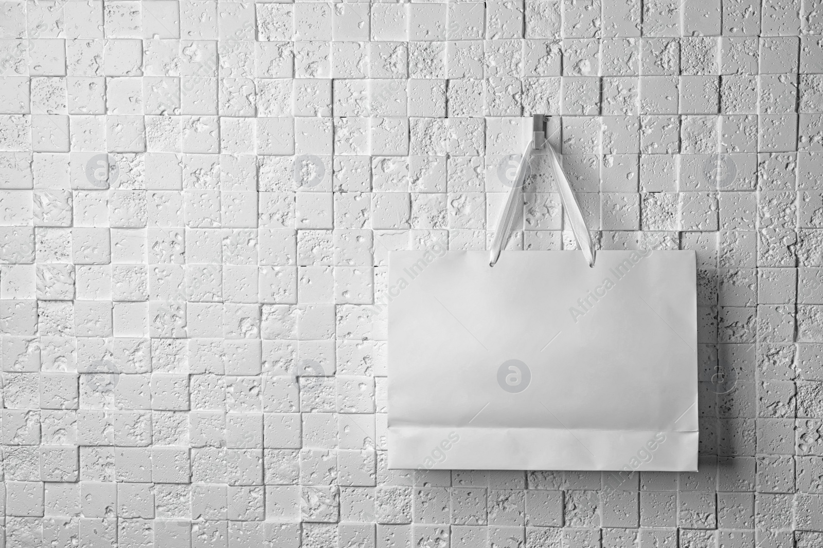 Photo of Paper shopping bag with ribbon handles hanging on white wall. Mockup for design