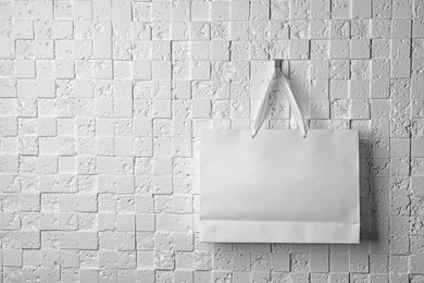 Photo of Paper shopping bag with ribbon handles hanging on white wall. Mockup for design