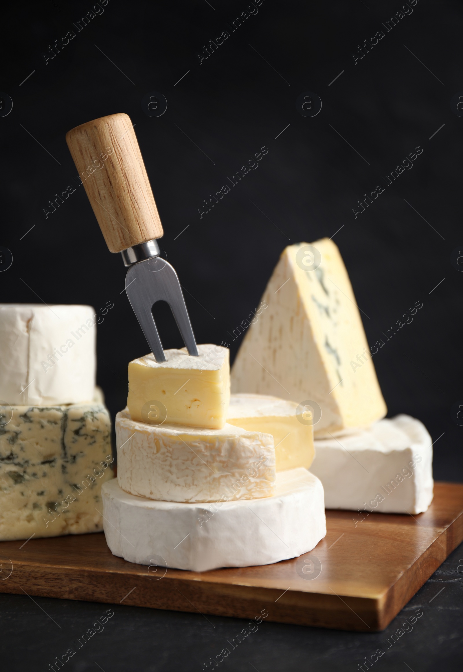 Photo of Different types of cheese and fork on black table