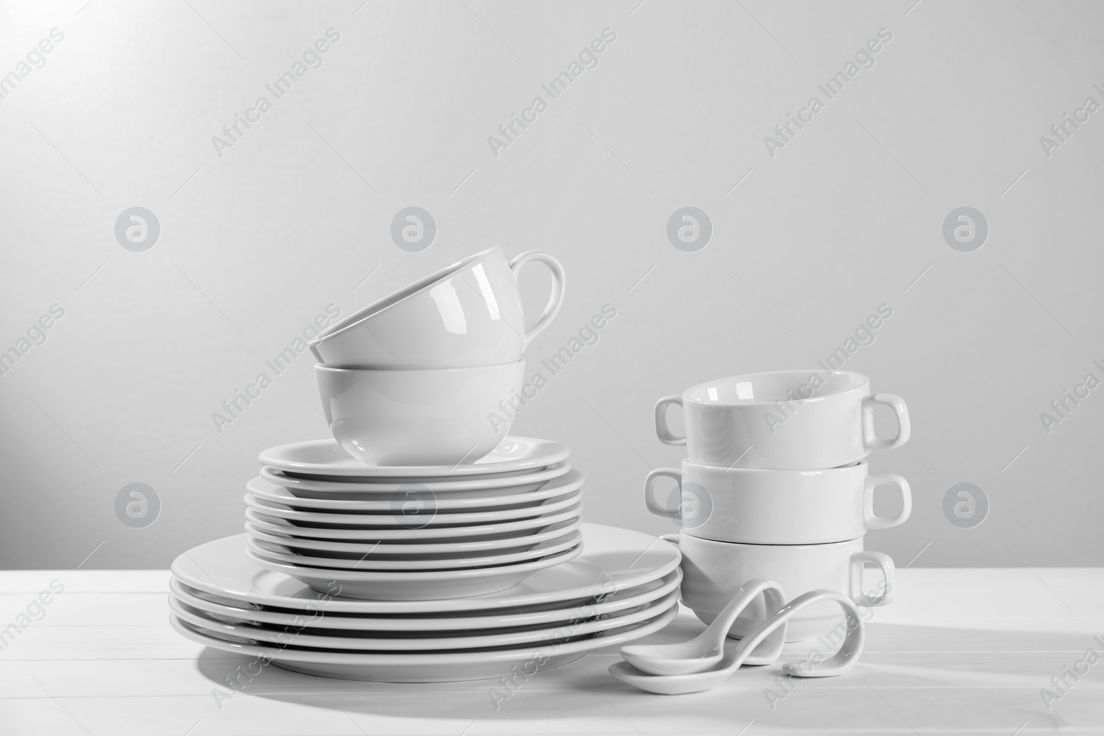 Photo of Set of clean dishware on white wooden table against light background